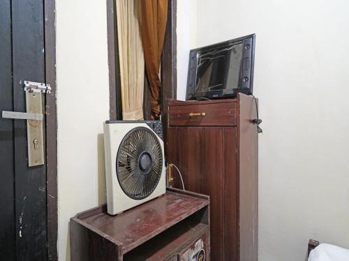 a television and a fan sitting on a wooden cabinet at SPOT ON 91783 Urban Syariah Residence in Bandung