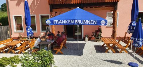 um grupo de pessoas sentadas numa mesa sob um guarda-chuva azul em Gasthaus Zum Schneider em Pottenstein