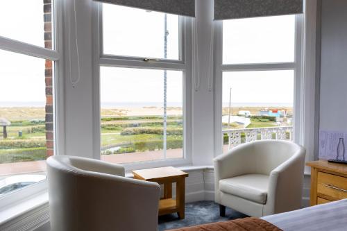 a bedroom with two chairs and a bed and windows at Furzedown Hotel in Great Yarmouth