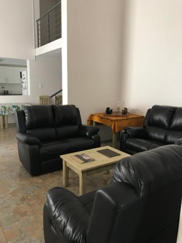 a living room with black leather couches and a coffee table at Livivane Guest House in Simunye