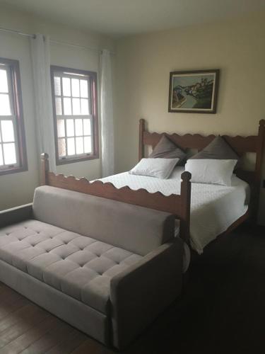 a bed and a couch in a bedroom with two windows at CASA RAIZ cama, café e prosa in Ouro Preto