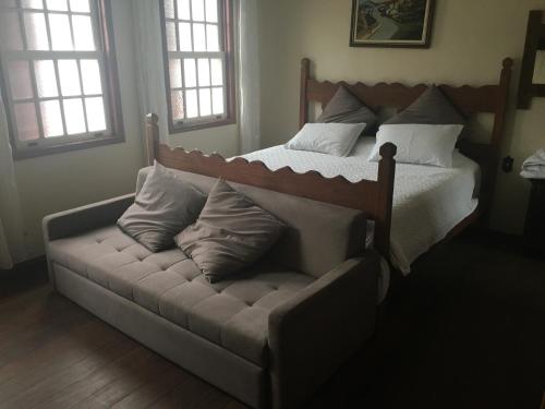 a bed with a couch in a room with windows at CASA RAIZ cama, café e prosa in Ouro Preto
