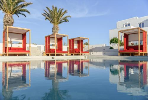 a swimming pool with red chairs and palm trees at Kallisti Paros in Naousa