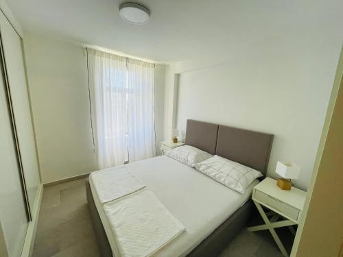 a small white bedroom with a bed and a window at Barbi Blue Apartments in Herceg-Novi