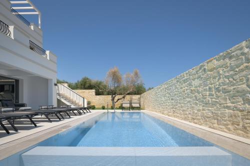 a swimming pool in front of a stone wall at Ivory Villa, with effusive design, By ThinkVilla in Perama