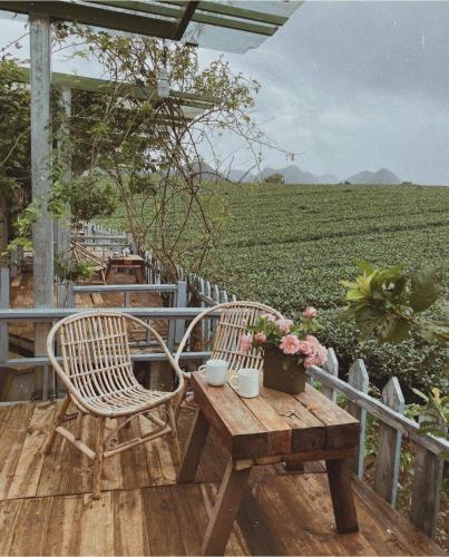 a wooden deck with two chairs and a table with flowers at Tiệm Cà Phê Mer Homestay & Coffee Mộc Châu in Mộc Châu