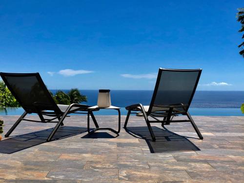 two black chairs sitting on a patio near the ocean at Habitation Caféière Samana Beauséjour - GUESTHOUSE in Pointe-Noire