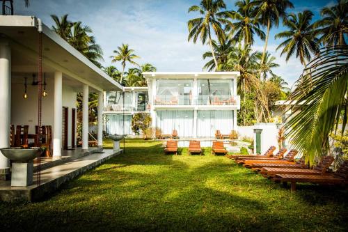 una casa con césped con sillas y palmeras en Infinity of Sri Lanka en Paiyagala South