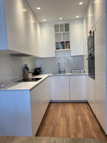 a white kitchen with white cabinets and a wooden floor at Ani’s apartment in Prishtinë