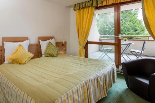 a bedroom with a bed with a chair and a balcony at Hotel Restaurant Le Petit Kohlberg in Lucelle