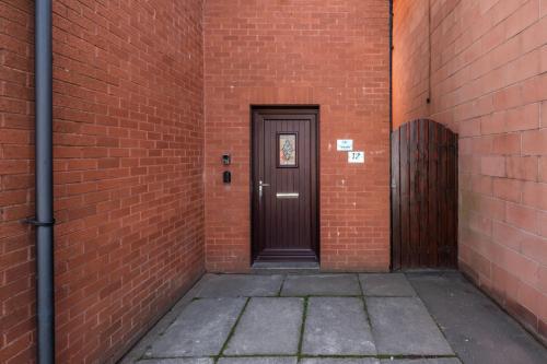 a brown door in a brick wall with a sidewalk at The Douglas - Spacious 2 bed apartment in Uddingston in Uddingston