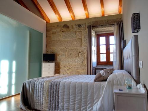 1 dormitorio con cama blanca y pared de piedra en A Cantaruxa Maruxa Turismo Rural, en Mondariz