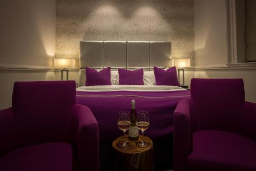 a bedroom with a purple bed with two glasses of wine at Barnett Hill Hotel in Guildford