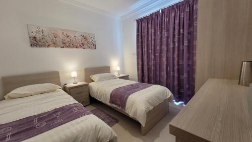 a bedroom with two beds and a window with purple curtains at Lovely Apartment with Side Sea View in St Paul's Bay