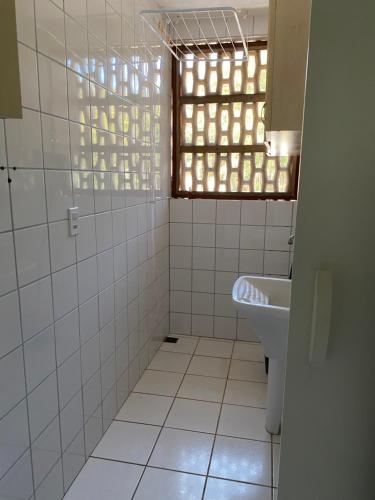 Baño de azulejos blancos con ventana y lavabo en Flores da Aldeia en Arraial d'Ajuda
