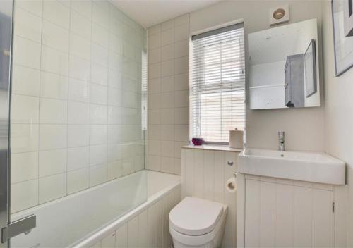 a white bathroom with a toilet and a sink at Crows Nest in Brancaster