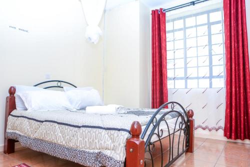 - une chambre avec un lit doté de rideaux rouges et d'une fenêtre dans l'établissement Baraka Homes, à Kisumu