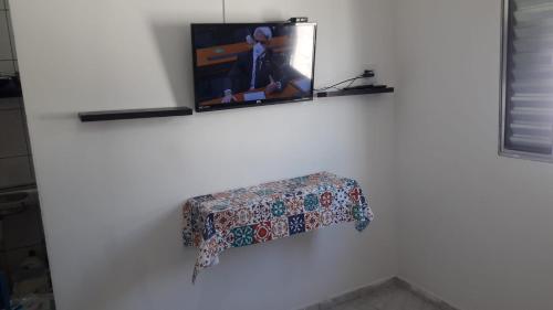 a tv hanging on a white wall with a table at Kit Ocian in Praia Grande