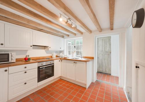 a kitchen with white cabinets and an orange tile floor at Lime Quay Cottage in Woodbridge