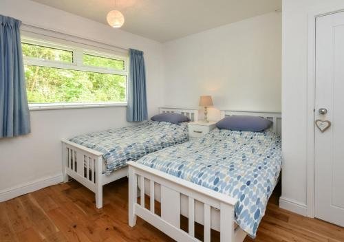 two beds in a bedroom with blue curtains and a window at 4 Glyn y Marian in Llanbedrog