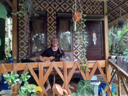 a woman sitting on a porch with a guitar at anik homestay & dormy Batukaras in Batukaras