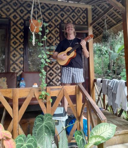 a man holding a guitar in front of a house at anik homestay & dormy Batukaras in Batukaras