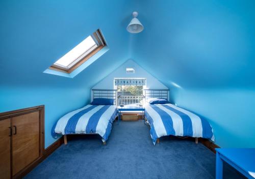 a blue bedroom with two beds and a window at Pelydryn in Abersoch