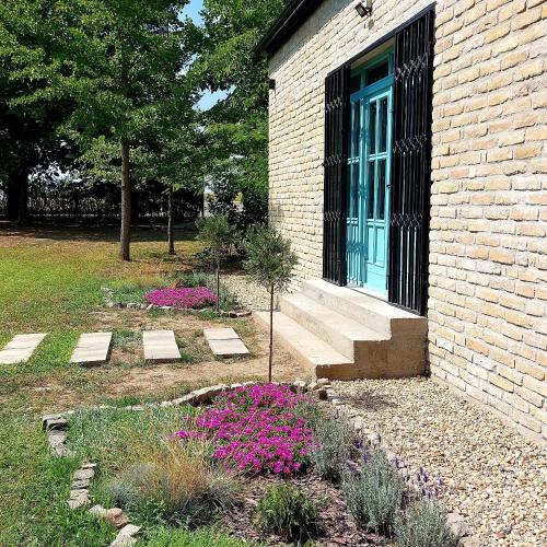a brick house with a blue door and purple flowers at Kuca 318 Cenej in Novi Sad