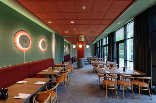 ein Restaurant mit Holztischen, Stühlen und Fenstern in der Unterkunft Mercure Hotel Gera City in Gera