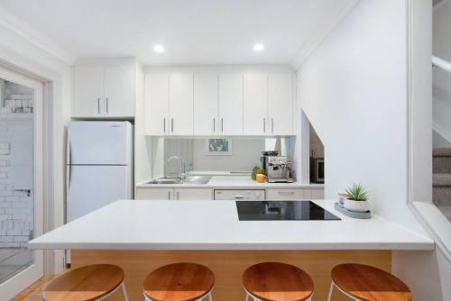 uma cozinha com um balcão branco e bancos de madeira em Modern Central China town Home - Free Carpark em Adelaide