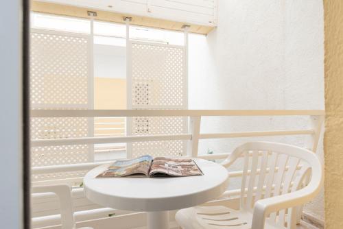 a white table and a white chair with a book on it at O7 Nordeste Playa in Can Picafort