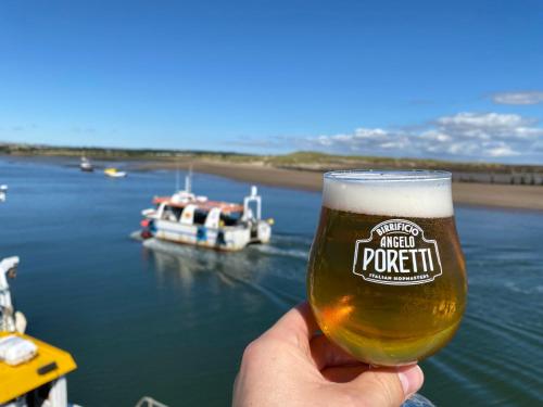 a hand holding a glass of beer with a boat in the water at Harbour Inn in Amble