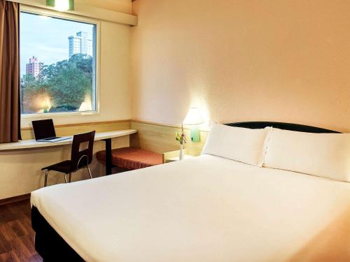 a hotel room with a bed and a desk and a window at ibis Santo Andre in Santo André