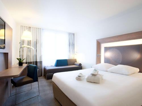 ein Hotelzimmer mit einem großen weißen Bett und einem Stuhl in der Unterkunft Novotel Basel City in Basel