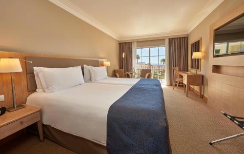 a hotel room with a large bed and a desk at Hotel Porto Santa Maria - PortoBay - Adults Only in Funchal