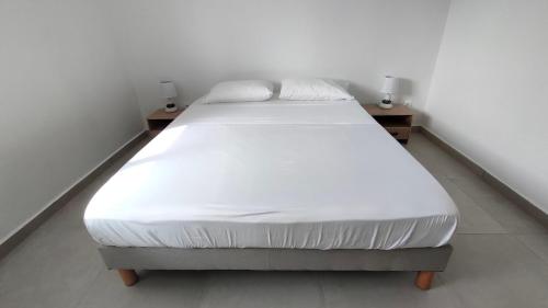 a white bed in a white room with two tables at Les Eaux Turquoise in Terre-de-Haut