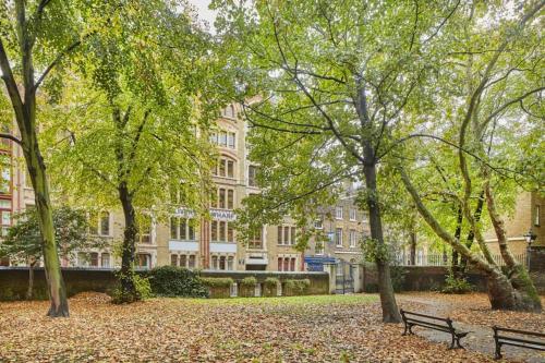 un parque con un banco y árboles frente a un edificio en City Riverview 1/2 Bedroom Apartment en Londres