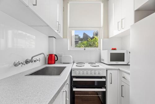 a white kitchen with a stove and a microwave at BROUG10W - City View Studio in Sydney