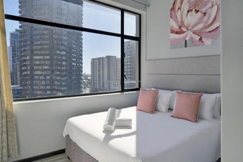 a bedroom with a large window and a white bed with pink pillows at The Heriot City Centre Apartments in Cape Town