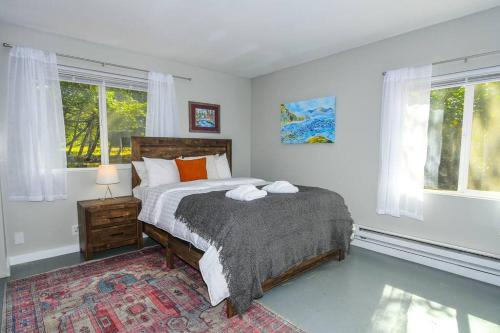 a bedroom with a bed and two windows at Adorable Cottage Among Trees Close To Everything in Vancouver