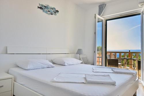a white bedroom with a bed with a view of the ocean at Guest House Marija in Bol