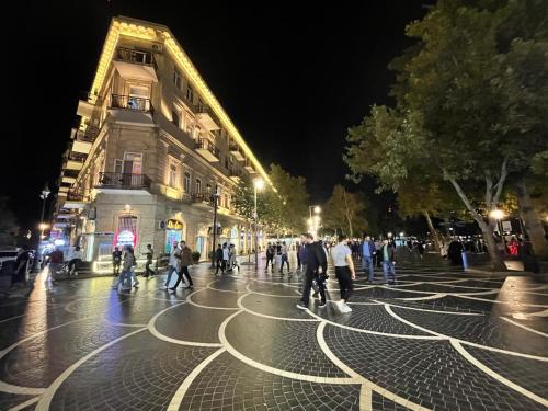 a group of people walking down a street at night at Fountain Square-Balconies in Old Town in Baku