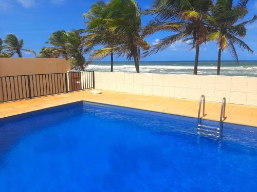 a blue swimming pool with the beach in the background at Village Praia do Flamengo frente mar in Salvador