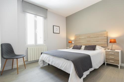 a white bedroom with a large bed and a chair at Apartamento Foro Romano in Zaragoza
