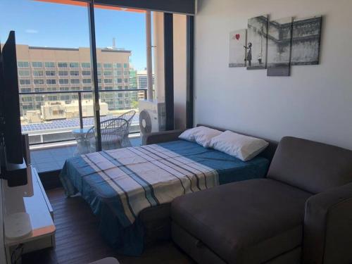 a bedroom with a bed and a couch and a window at Tindy’s City Pad in Adelaide