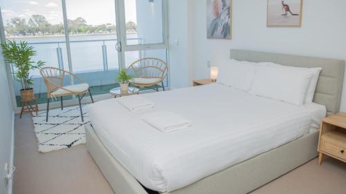 a bedroom with a large white bed and two chairs at Bridgepoint 103 in Mandurah