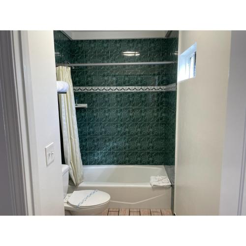 y baño con aseo y ducha de azulejos verdes. en Oak Tree Inn en Los Ángeles