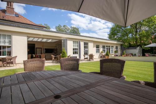 a wooden table with chairs and an umbrella in a yard at The Pheasant Hotel, Holt, Norfolk - The Coaching Inn Group in Kelling