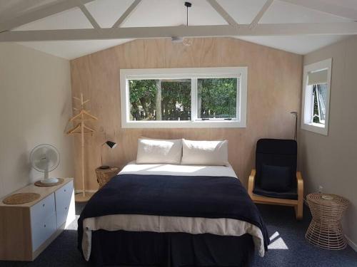 a bedroom with a bed and a chair and a window at Beach Break Cabin - short walk to beach and cafes in Waihi Beach