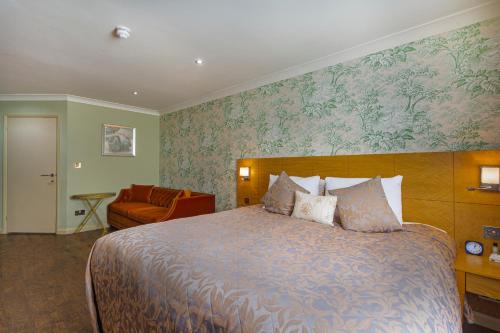 a bedroom with a large bed and a chair at The Pheasant Hotel, Holt, Norfolk - The Coaching Inn Group in Kelling